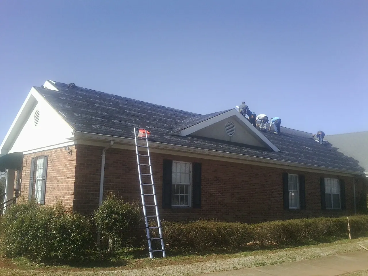 Crew tearing shingles off a brick ranch roof with a ladder set — Metal Roof Repair work by our crew in Columbus