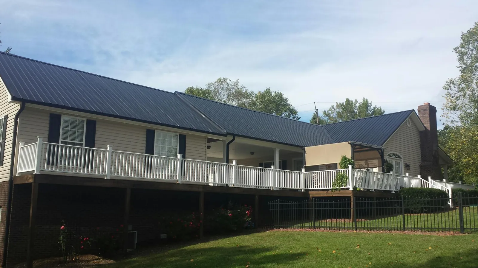 Black metal roof above a long white railed deck on a hillside home in Columbus
